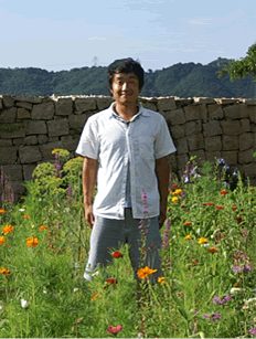 花が咲く庭に立つ代表の鈴木稔也さん